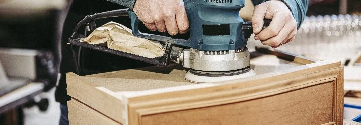 Person schleift Holz mit einem Schwingschleifer